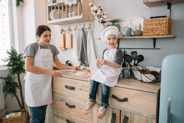 Young happy mom and her baby cook cookies at home in the kitchen. Christmas Homemade Gingerbread. cute boy with mother in white uniform and hat cooked chocolate cookies - Foto, Bild