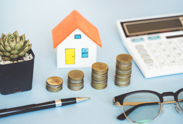 Σπίτι μοντέλο, κέρμα και αριθμομηχανή σε μπλε φόντο για τη χρηματοδότηση τραπεζική έννοια. - Φωτογραφία, εικόνα
