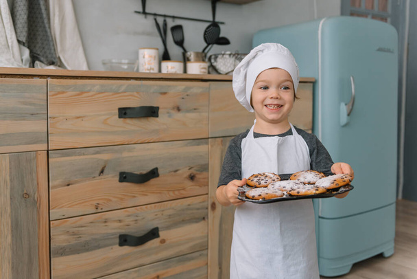 Young happy mom and her baby cook cookies at home in the kitchen. Christmas Homemade Gingerbread. cute boy with mother in white uniform and hat cooked chocolate cookies - Фото, зображення