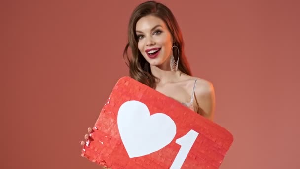 Cheerful pretty woman in bright sequins dress posing with unusual blank board over red background - Filmagem, Vídeo