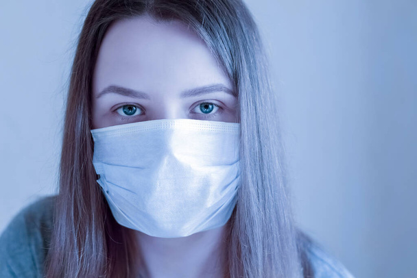 Sad young woman with protection medical mask looking at camera. Stay at home for quarantine to prevent coronavirus spread. Concept for protect from infection, respiratory disease, virus or bacteria. - 写真・画像