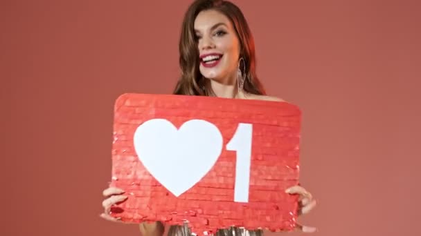Joyful pretty woman in bright sequins dress posing with unusual blank board and looking at the camera over red background - Footage, Video