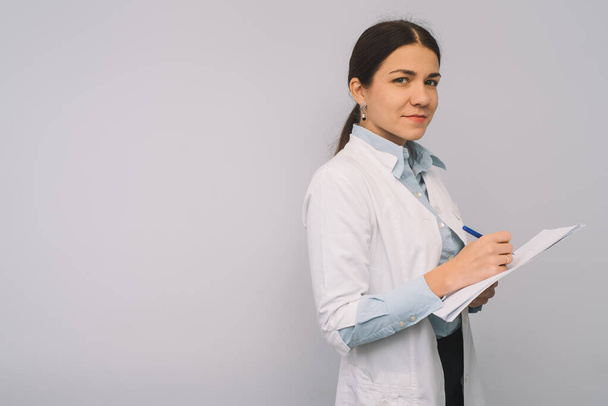 Female doctor in white uniform is holding flasks while standing against white background. - Fotoğraf, Görsel