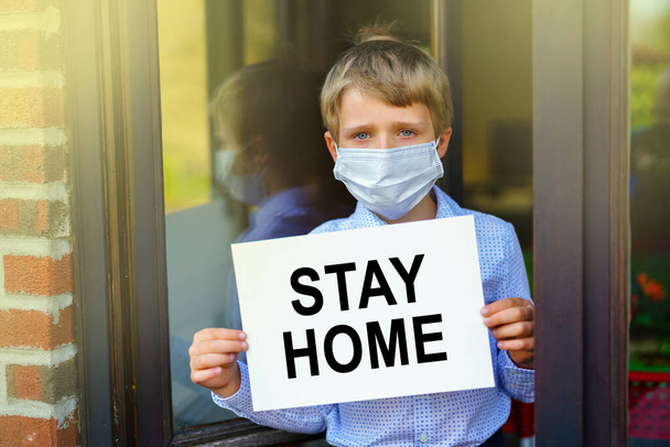 portrait of little boy wearing face mask holding banner with text Stay Home, Coronavirus pandemic worldwide crisis - Valokuva, kuva