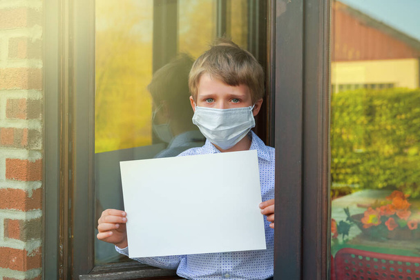portré a kisfiú arcmaszkot visel kezében üres fehér banner, Coronavirus pandémia világméretű válság - Fotó, kép