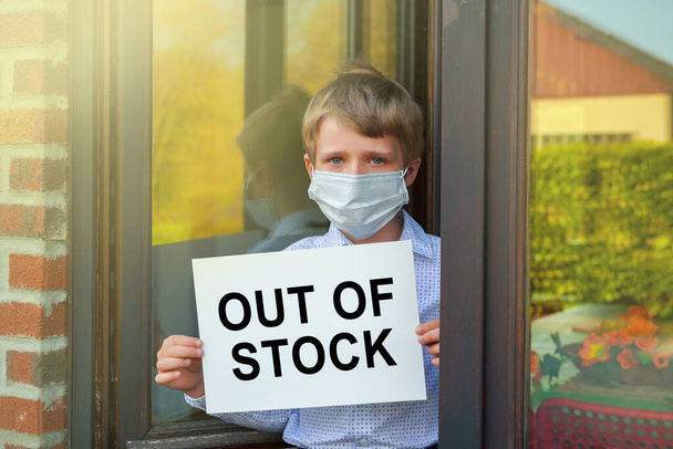 portrait of little boy wearing face mask holding banner with text Out Of Stock, Coronavirus pandemic worldwide crisis - Photo, Image