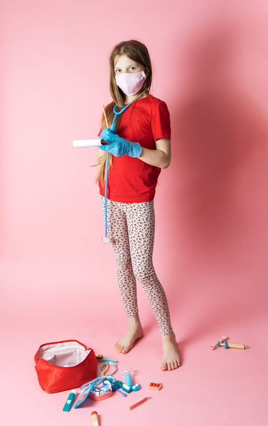 Personal protective equipment: a teenage girl in a medical mask and blue gloves plays a nurse. Portrait on a pink background. - Foto, afbeelding