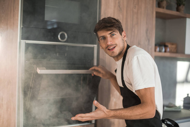 frustrated young man standing near broken oven - Foto, Imagen