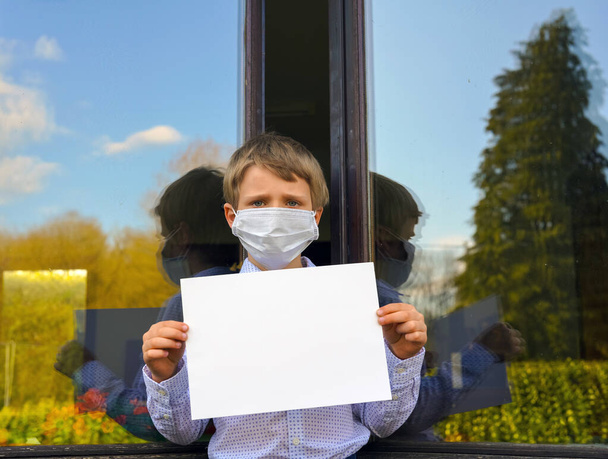 portré a kisfiú arcmaszkot visel kezében üres fehér banner, Coronavirus pandémia világméretű válság - Fotó, kép