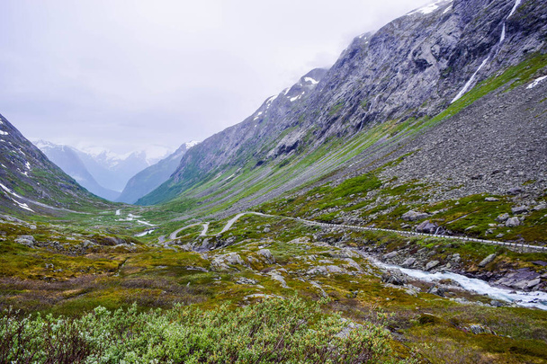 Die Straße verläuft im Tal zwischen hohen Bergen mit schneebedeckten Gipfeln, in denen sich die Gletscher des Nationalparks Jostedalsbreen befinden. Stryn im Kreis Vestland. In Norwegen unterwegs. - Foto, Bild