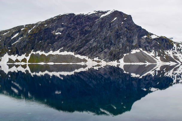 The lake with pure meltwater, formed as a result of melting snow and glacier. Global warming, climate change. Beautiful reflection of rocks in calm water. - Zdjęcie, obraz
