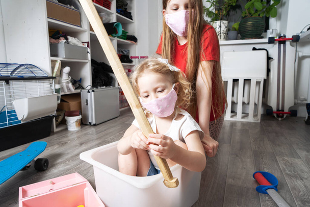 家にいる:医療用マスクの子供たちはおもちゃで遊び、白い箱に乗っています。家族生活の肖像画. - 写真・画像