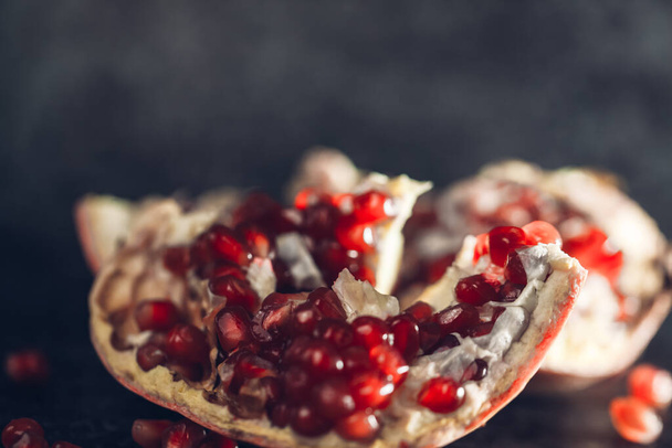 An open pomegranate (fruit) lies on the table on a gray background with a green branch - Foto, Imagem