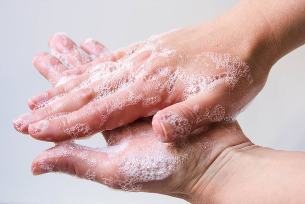 Hygiëne en bescherming van de handen tegen virussen (coronavirus) en bacteriën die zeep gebruiken. Vrouwen handen met geschuimde zeep close-up op een witte achtergrond. Het proces van het goed wassen van handen met zeep. - Foto, afbeelding