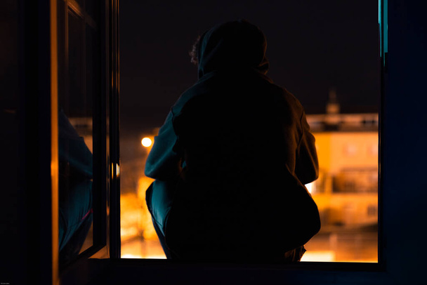 Πρόσωπο που συλλογίζεται στο σπίτι του που κάθεται στο παράθυρο σε καραντίνα για τον κορωναϊό - Φωτογραφία, εικόνα