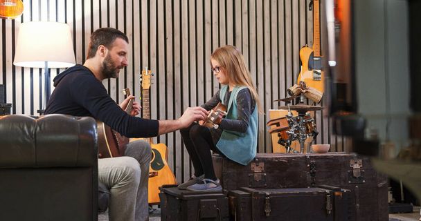 Dad teaching guitar and ukulele to his daughter.Little girl learning guitar at home.Side view.Ukulele class at home. Child learning guitar from her father - Foto, imagen