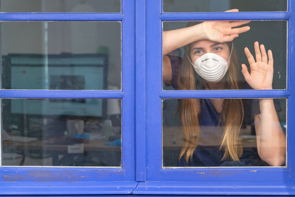 Koronawirus. Chora kobieta z wirusem korony patrząca przez okno, nosząca maskę ochronną i wyleczająca się z choroby w domu. Kwarantanna. Pacjent odizolowany, by zapobiec infekcji. Dom. - Zdjęcie, obraz