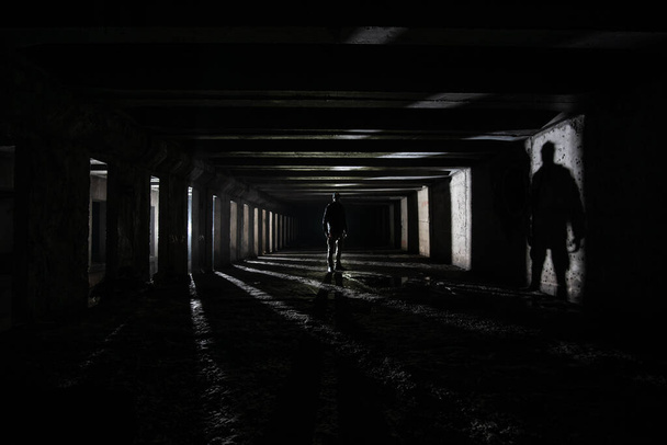 Shilouette και σκιά του ανθρώπου υπόγεια εξερευνητής σε εγκαταλελειμμένο σκοτεινό τούνελ. - Φωτογραφία, εικόνα
