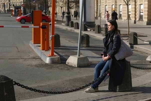 Saint-petersburg, Russia - 7 aprile 2020:: Nevsky Prospekt, Vosstaniya Square. Una donna stanca in cappotto nero seduta sul marciapiede vicino alla stazione ferroviaria di Mosca
 - Foto, immagini