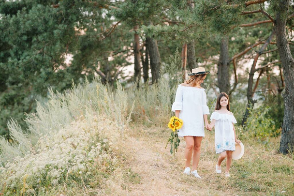 Fröhliche Mutter und ihre kleine Tochter amüsieren sich im sommerlichen Hintergrund. Glückliche Familie im Hintergrund der Natur. Nette Mädchen mit bunten Blumen. - Foto, Bild