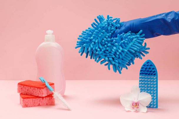 Plastik bulaşık deterjanı, sünger, fırça ve pembe arka planda bir bez parçası tutan kauçuk eldivenli bir el. Yıkama ve temizleme seti. - Fotoğraf, Görsel