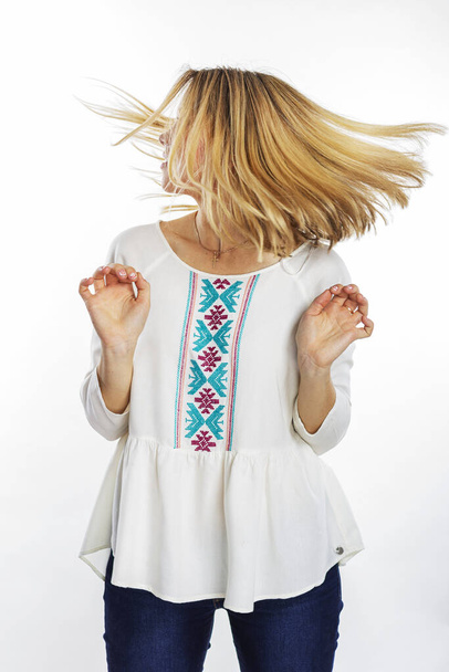 Isoliertes Porträt eines blonden Mädchens mit fliegendem Haar. Bob Haarschnitt. Lächelndes Mädchen in einer weißen bestickten Bluse. - Foto, Bild