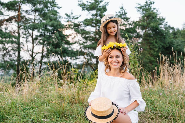 Cheerful mother and her little daughter having fun together in the summer background. Happy family in the nature background. Cute girls with colorful flowers. - Foto, Imagem