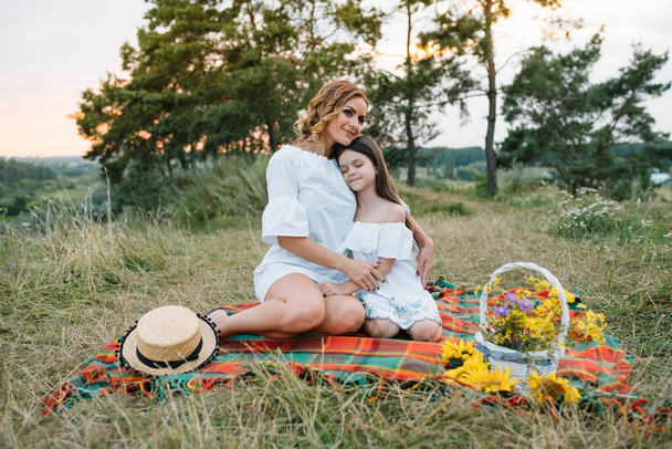 Fröhliche Mutter und ihre kleine Tochter amüsieren sich im sommerlichen Hintergrund. Glückliche Familie im Hintergrund der Natur. Nette Mädchen mit bunten Blumen. - Foto, Bild