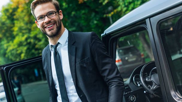 Handsome smiling young businessman coming out of his car while standing outdoors - Foto, afbeelding