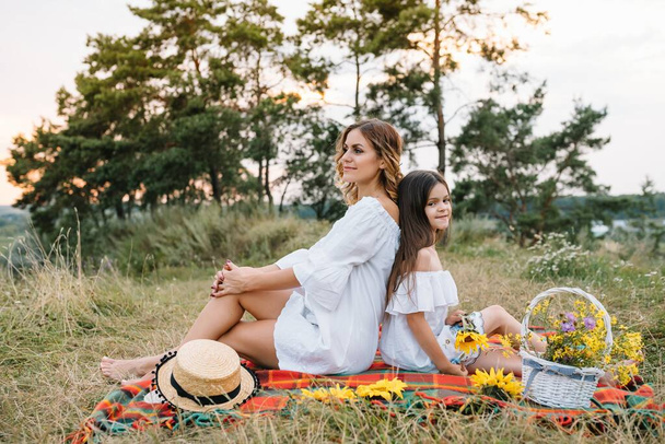 Cheerful mother and her little daughter having fun together in the summer background. Happy family in the nature background. Cute girls with colorful flowers. - Foto, afbeelding