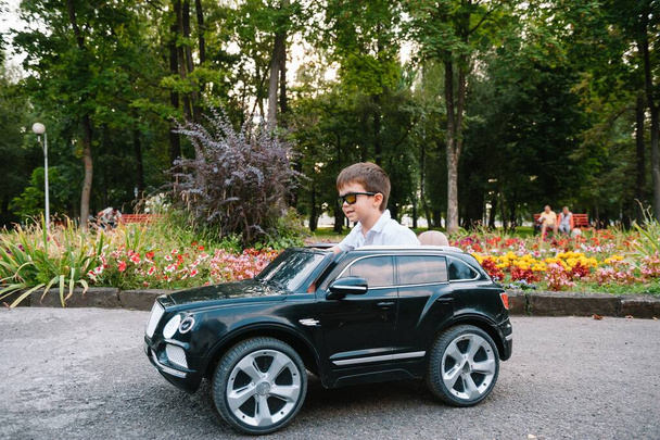 Lindo chico en montar un coche eléctrico negro en el parque. Chico gracioso monta en un coche eléctrico de juguete. Pequeño niño feliz montando un coche eléctrico negro en el parque. Copiar espacio
. - Foto, imagen