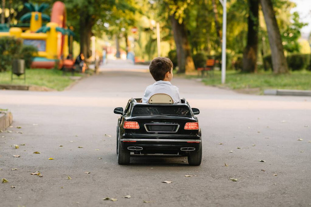 Cute boy in riding a black electric car in the park. Funny boy rides on a toy electric car. little happy boy riding a black electric car in the park. Copy space. - Photo, image