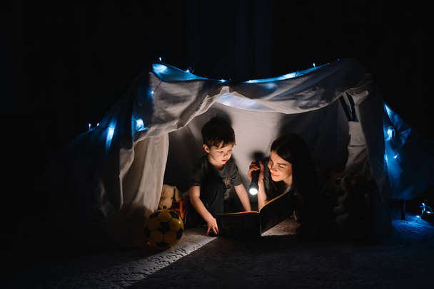 happy family mother and child son reading a book with a flashlight in a tent at home. family concept - Fotó, kép