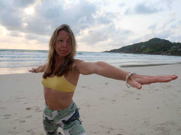 Mladá běloška žena praxe jóga bojovník pózovat při západu slunce pobřeží. - Fotografie, Obrázek