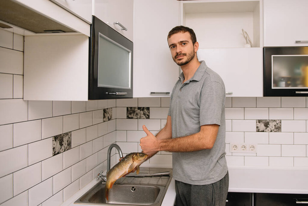 Man cutting fresh fish in kitchen in home. Man butchering fish for cook - Foto, afbeelding