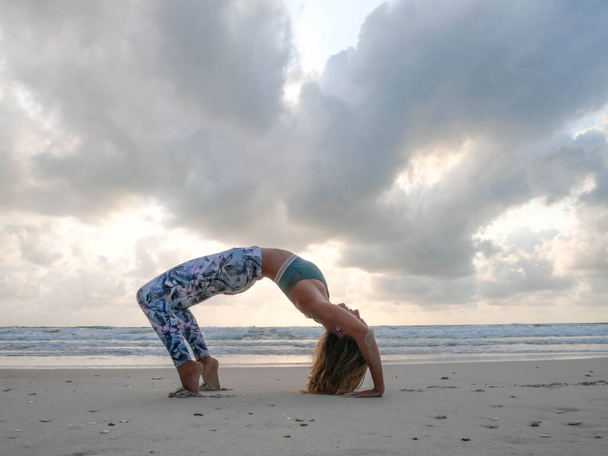 Молода гнучка дівчина практикує колесо йоги позує на морі під час заходу сонця
. - Фото, зображення