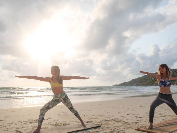 Deux femmes pratiquent la posture de yoga guerrier au coucher du soleil bord de mer
 - Photo, image