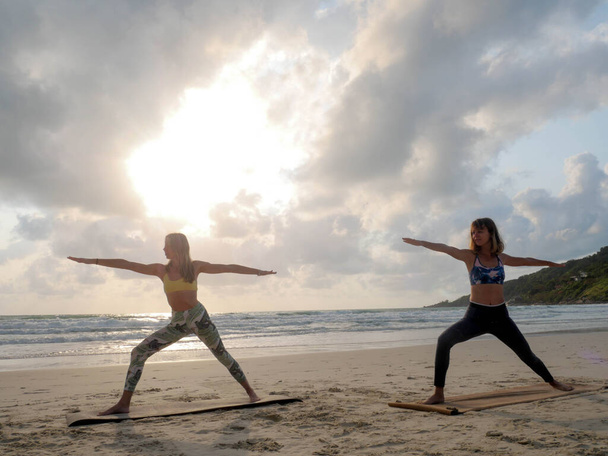 Kaksi naista harjoittaa soturi jooga Asana auringonlaskun meren rannalla
 - Valokuva, kuva