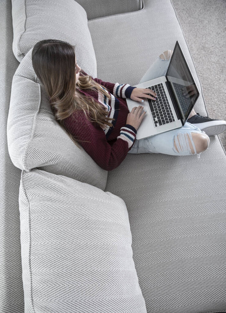 Teini tyttö opiskelee kotona kannettavan tietokoneen avulla, istuu mukavalla sohvalla
. - Valokuva, kuva