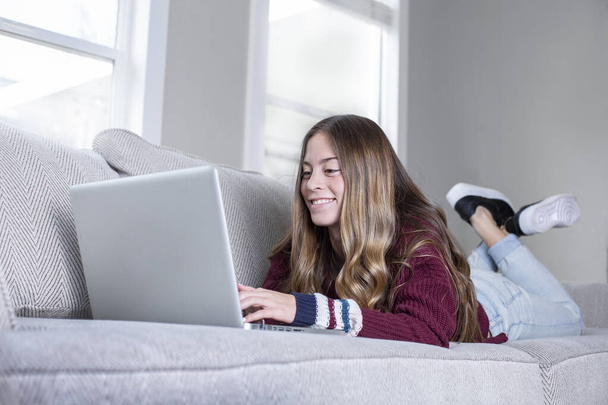 Ragazza adolescente che studia a casa usando il computer portatile, sdraiato sul divano
. - Foto, immagini