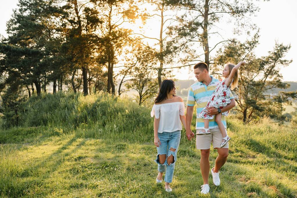 Happy family walking in the park. Mom, dad and daughter walk outdoors, parents holding the baby girl's hands. Childhood, parenthood, family bonds, marriage concept - Foto, Bild
