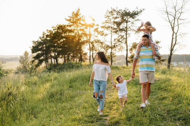 Color photo of smiling young parents and two children, rest and have fun in nature. Love, family and happy childhood lifestyle concept - Foto, afbeelding