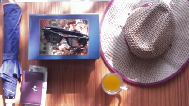 Vista superior de la playa de fondo de verano accesorios de viaje para mujeres. Gafas de sol, monedero, libros, paraguas, sombrero de paja y un vaso de jugo. Concepto de vacaciones de verano con espacio de copia para texto. - Metraje, vídeo