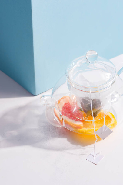 Nyári házi hideg gyümölcs tea ital egy üveg átlátszó teáskanna egy fehér asztalon árnyékkal pasztell kék fal. - Fotó, kép