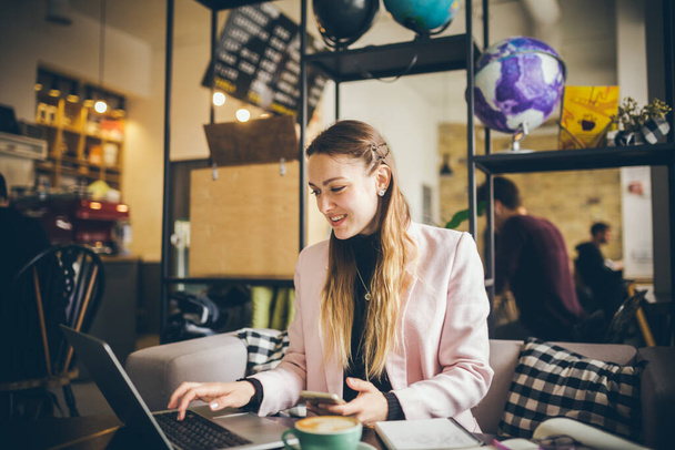 Piękna młoda freelancer kobieta za pomocą laptopa siedzi przy stole Cafe. Bizneswoman ręcznie wpisując tekst, za pomocą kontaktów z laptopem informacji biznesowych wyszukiwania. Pretty kobieta freelancer pracy kawiarnia. - Zdjęcie, obraz