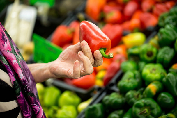 Grandma, the old woman chooses pepper in the supermarket. hands. - Photo, Image