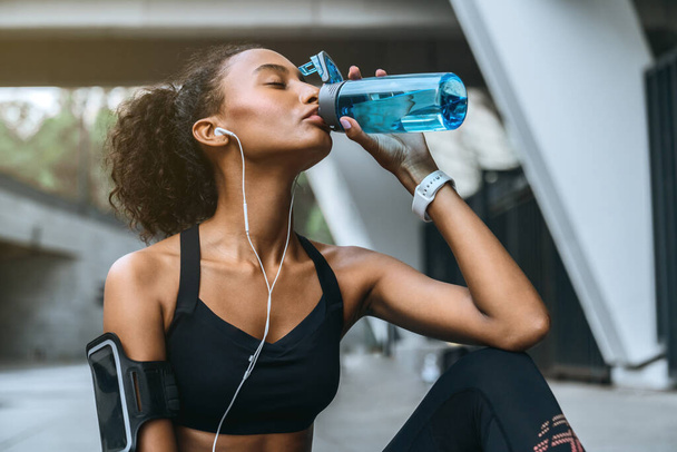 African fitness woman drinking water from bottle after workout outdoors - Foto, Bild
