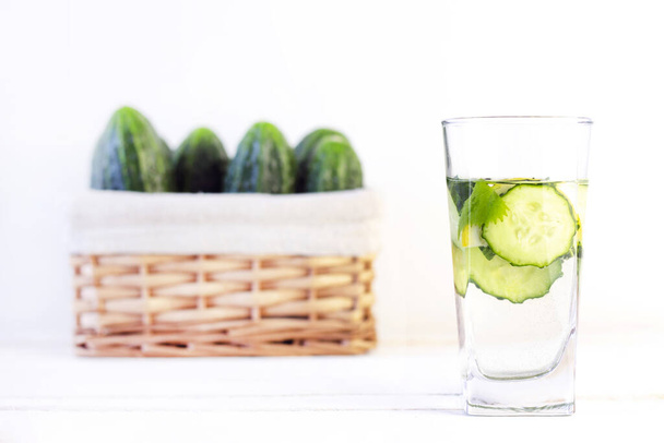 Health care, fitness, healthy eating concept. Fresh cool lemon cucumber drink with water, cocktail, detox drink, lemonade in a glass jug and a glass. wicker basket with cucumbers - Photo, image