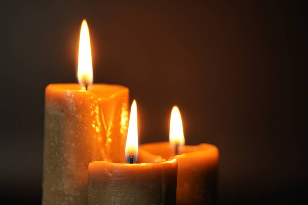 Gruppe von drei braunen brennenden Kerzen auf schwarzem Hintergrund in Großaufnahme. Konzept von Komfort, Romantik, Mystik, Okkultismus, Religion, ein Symbol der Erinnerung.. - Foto, Bild