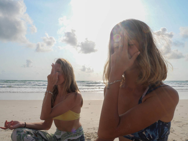 Twee yoga meisjes maken nadi shodhana pranayama therapeutische oefening in zonlicht. - Foto, afbeelding
